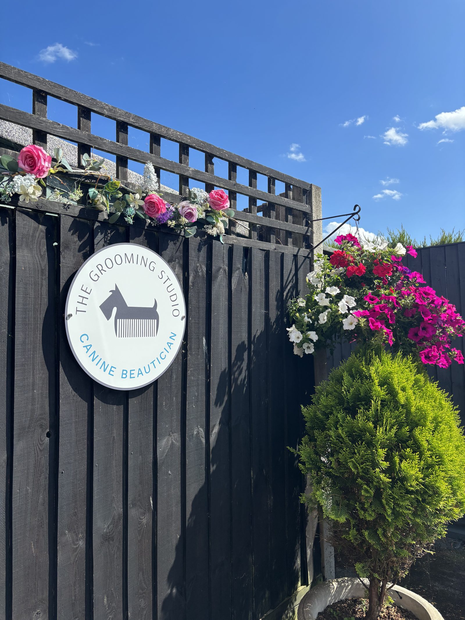 The Grooming Studio sign on the garden gate in Holyport, framed by flowers